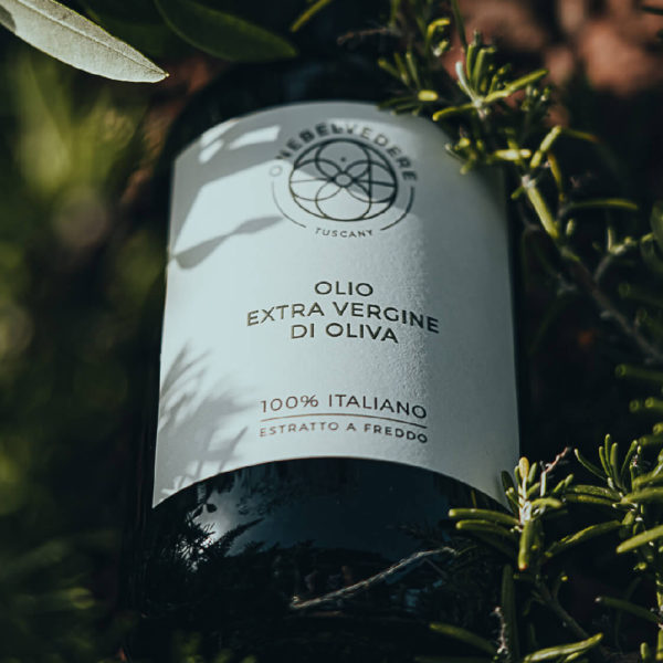 A bottle of Olive oil from One Belvedere laying on the ground surrounded by plants