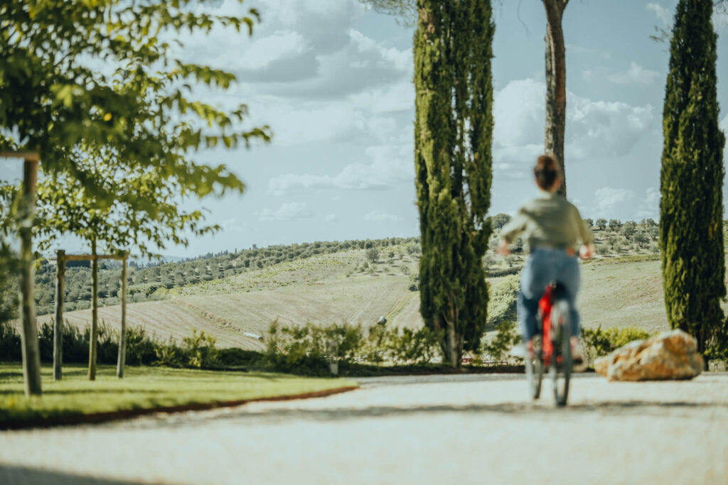 A guest bikes through the scenic Tuscany landscape at One Belvedere Tuscany, surrounded by rolling hills, vineyards, and picturesque views, showcasing an adventurous outdoor experience.