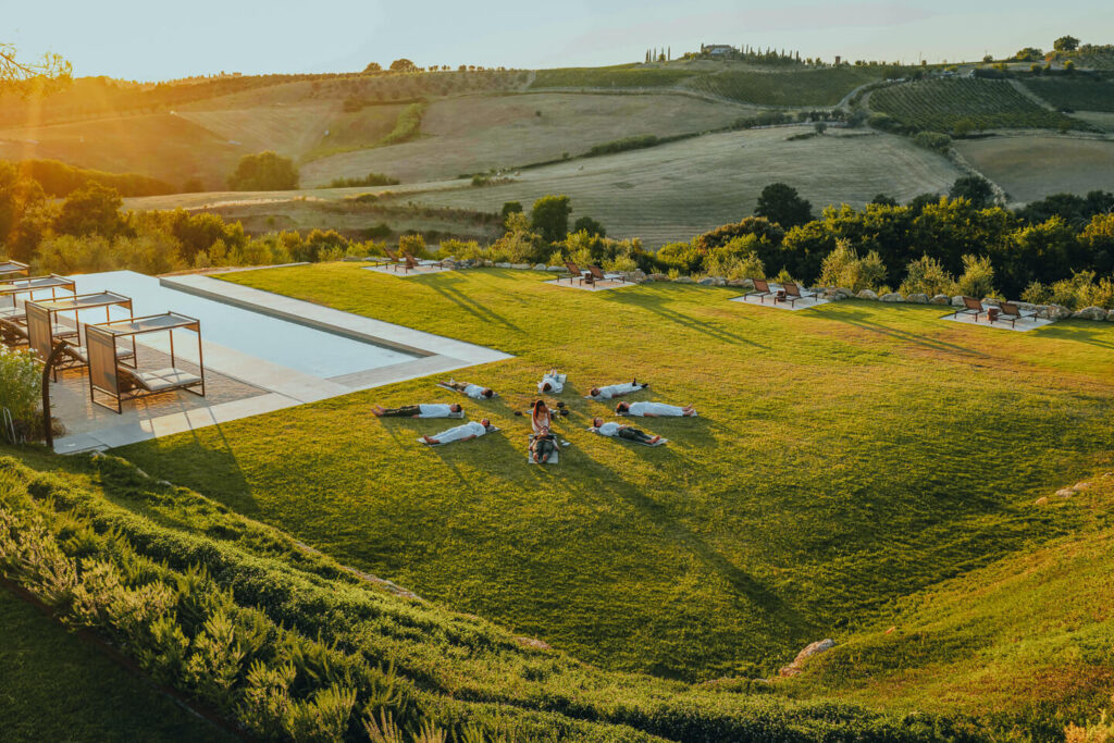 Group sound healing session at sunset on the lawn beside the infinity pool at One Belvedere Tuscany, surrounded by rolling vineyards and scenic countryside views.