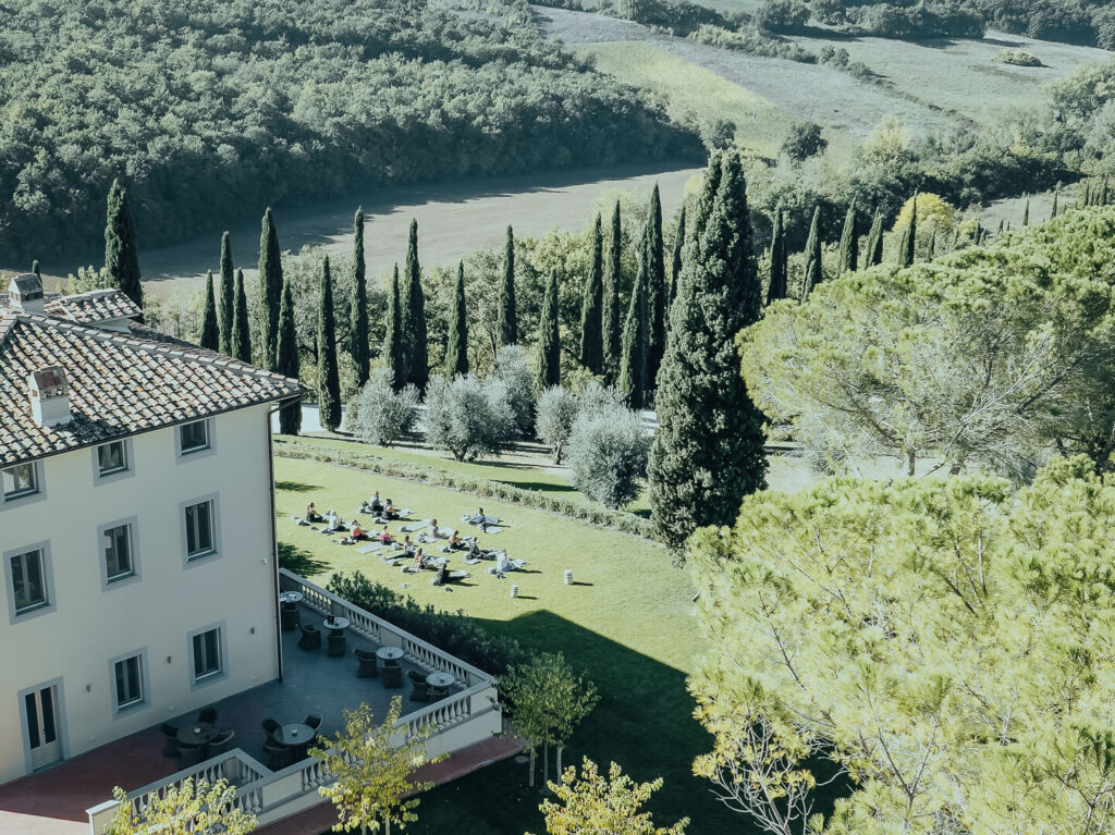 Guests enjoying a mindful outdoor yoga session on the grounds of One Belvedere Tuscany, surrounded by cypress trees and peaceful countryside views.