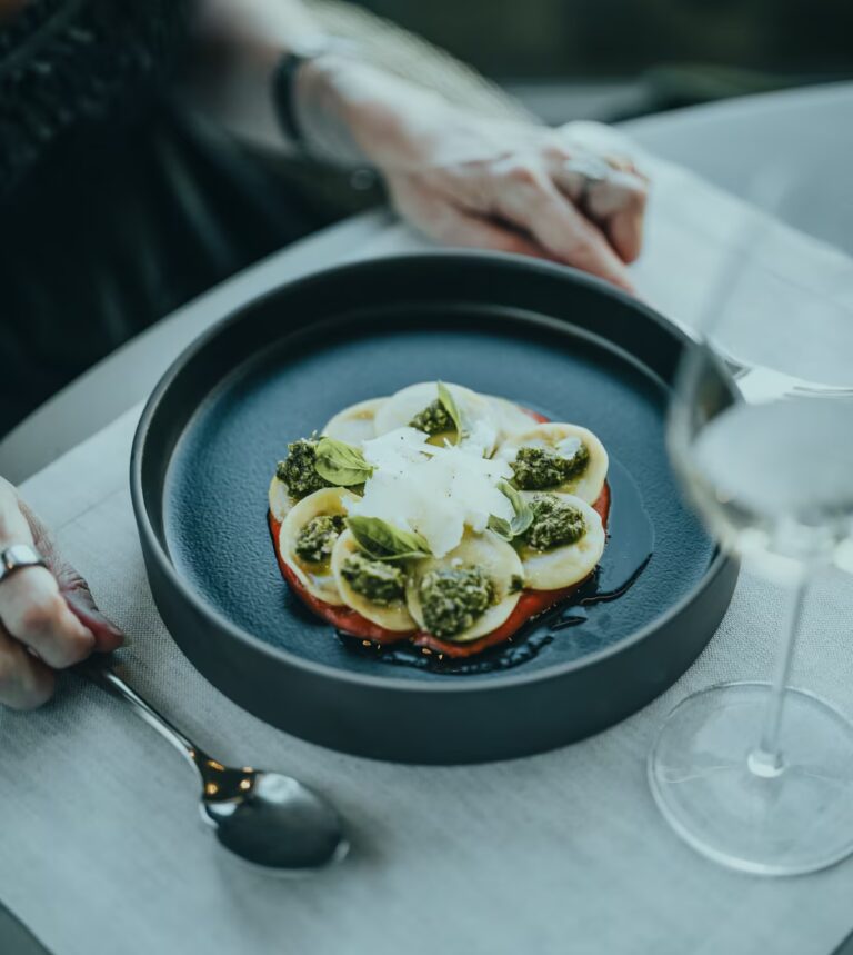 Authentic Tuscan food featuring handcrafted vegetarian pasta with basil pesto, shaved cheese, and fresh herbs.