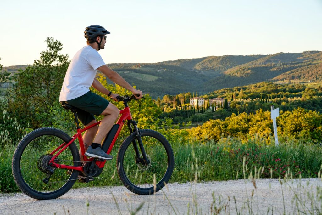 Man riding a red e-bike along a countryside path overlooking rolling Chianti hills and a cypress-lined Tuscan estate.
